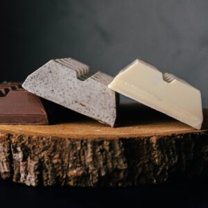 Assorted delicious sweet chocolate bars served on wooden tray against blurred gray background in studio